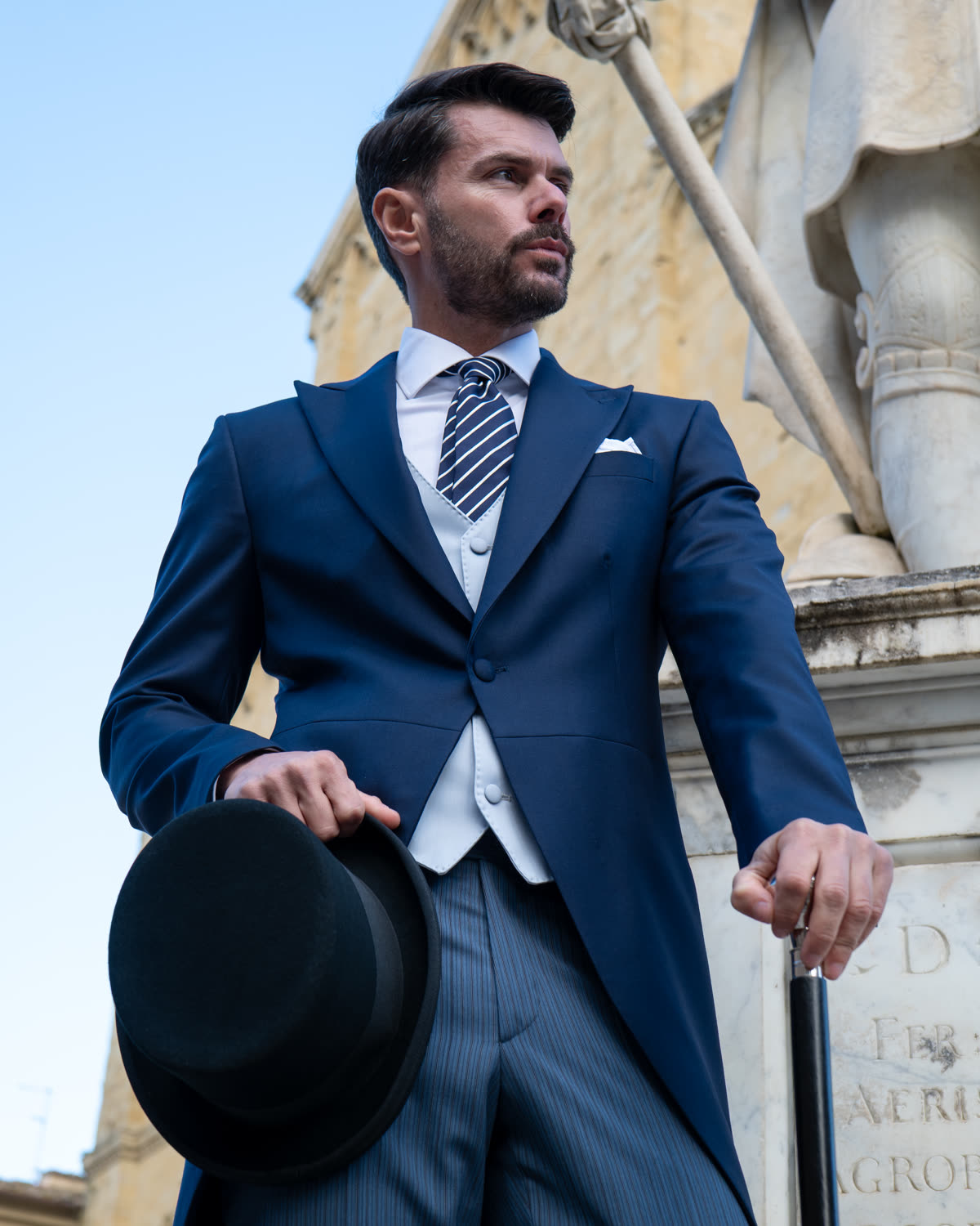 Uomo con tight lungo blu, gilet a righe, cilindro e bastone da passeggio